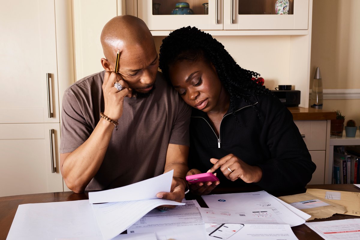 A couple going over bills with a phone calculator at their kitchen table