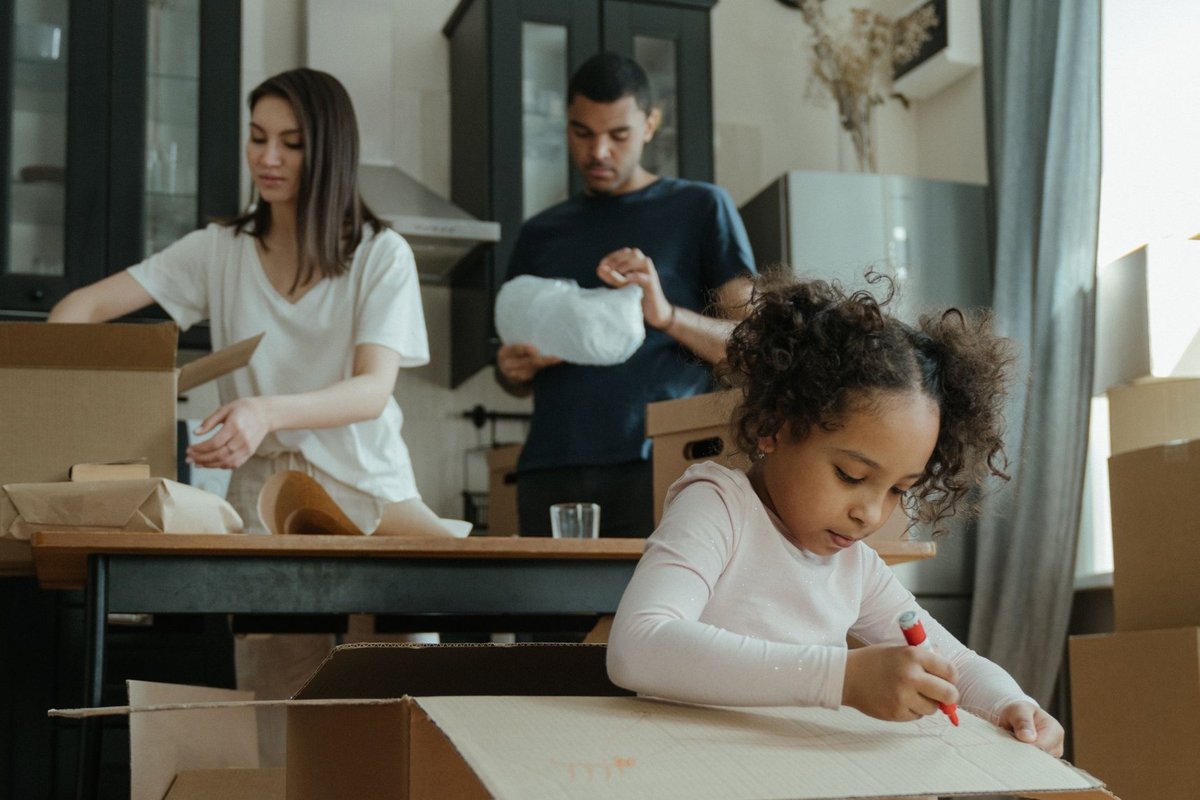 A family unpacking moving boxes in their kitchen while their daughter draws on a box