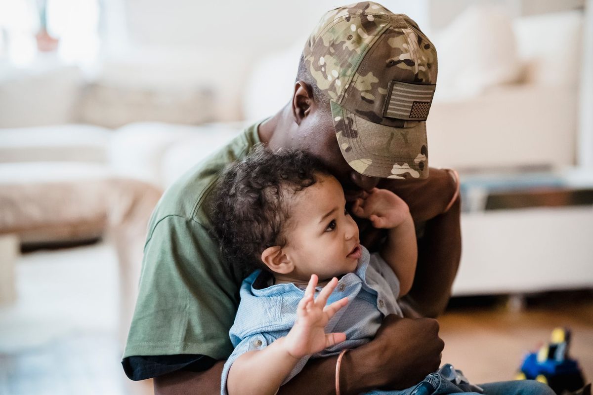 A man in a camouflage cap holding his young son at home
