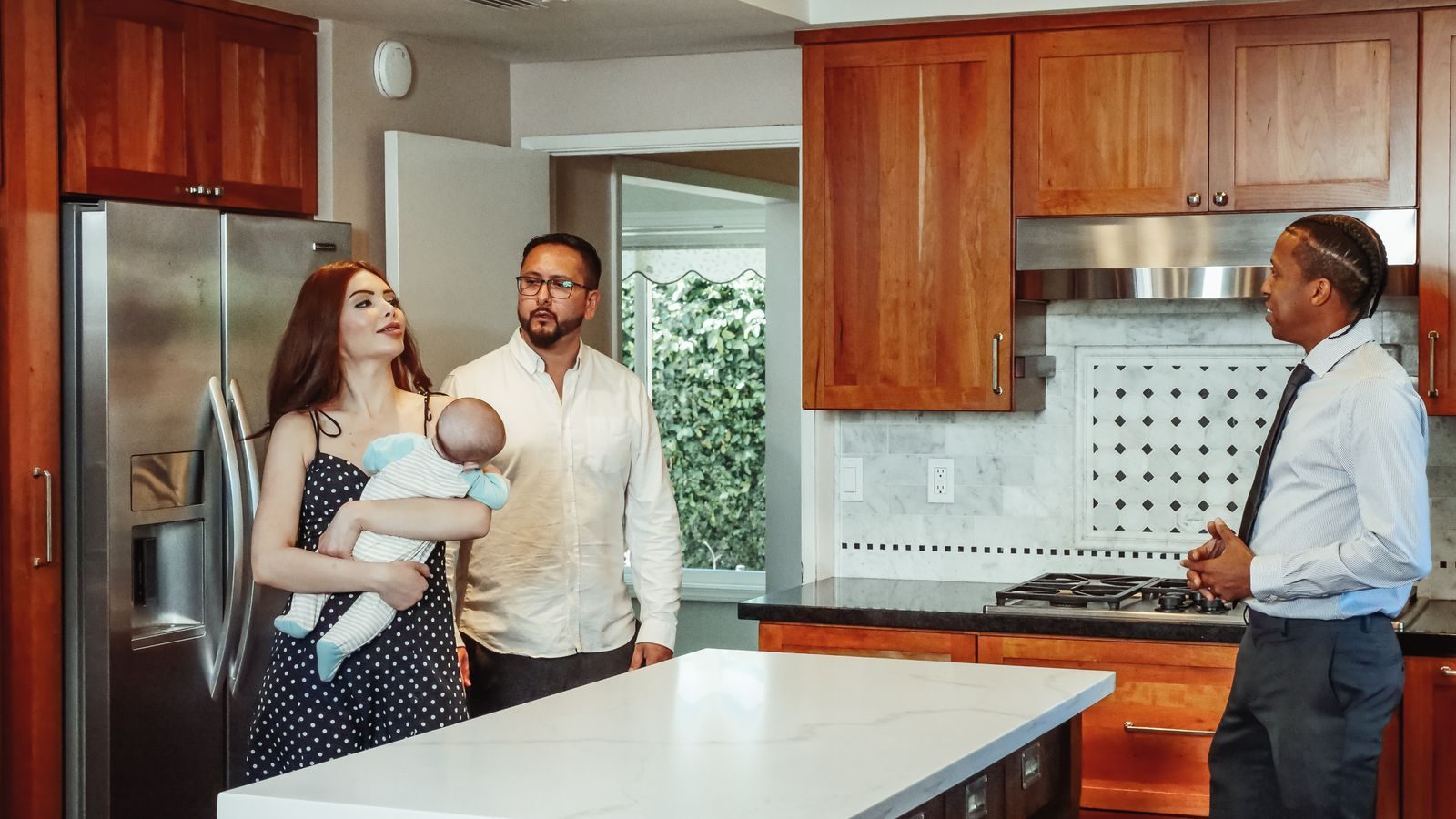 A young couple holding their baby while touring a kitchen